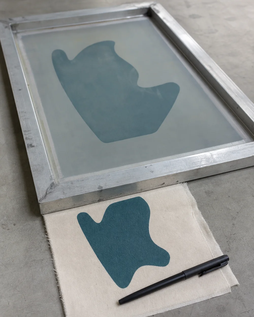 A screen frame and a fabric sample on a sampling bench with a pen laid beside them